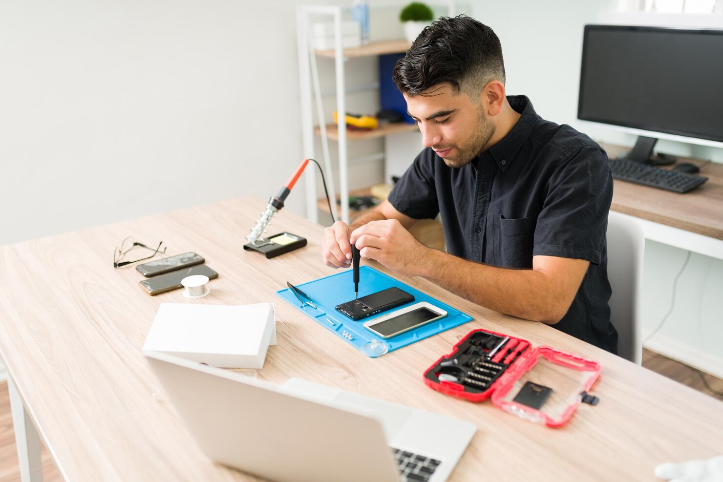 joven-sonriendo-mientras-repara-viejo-telefono-inteligente-tecnico-sexo-masculino-que-usa-destornillador-arreglar-telefono-celular-roto-taller