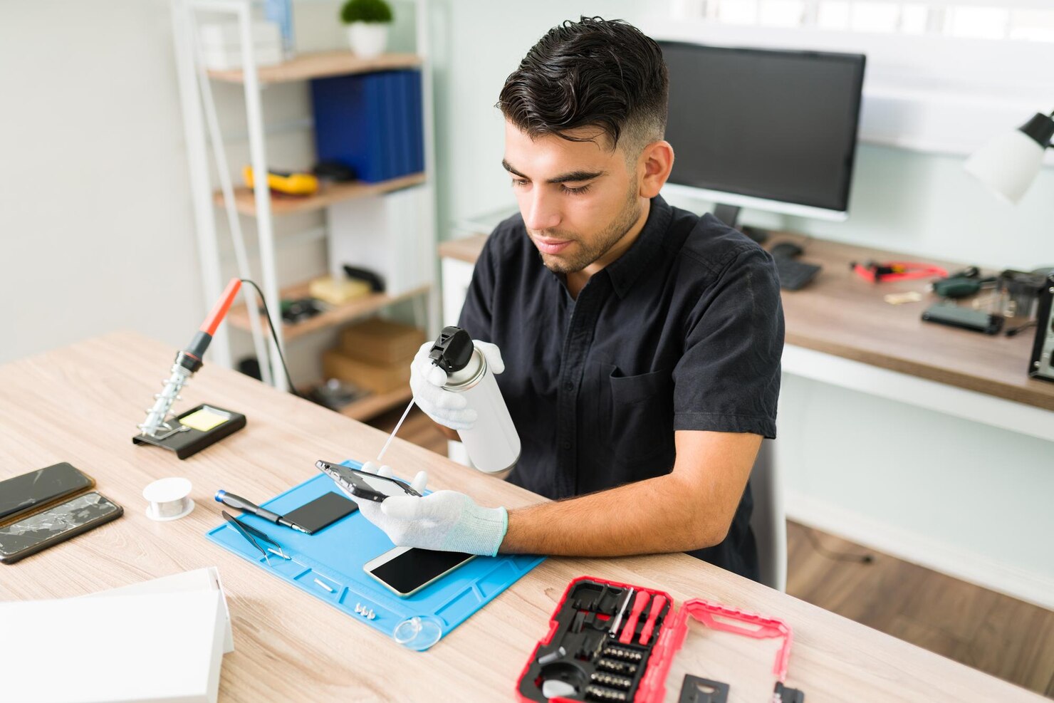 joven-tecnico-masculino-que-usa-aire-comprimido-limpiar-dentro-telefono-inteligente-sucio-taller-reparacion-hombre-latino-guantes-limpiando-celular